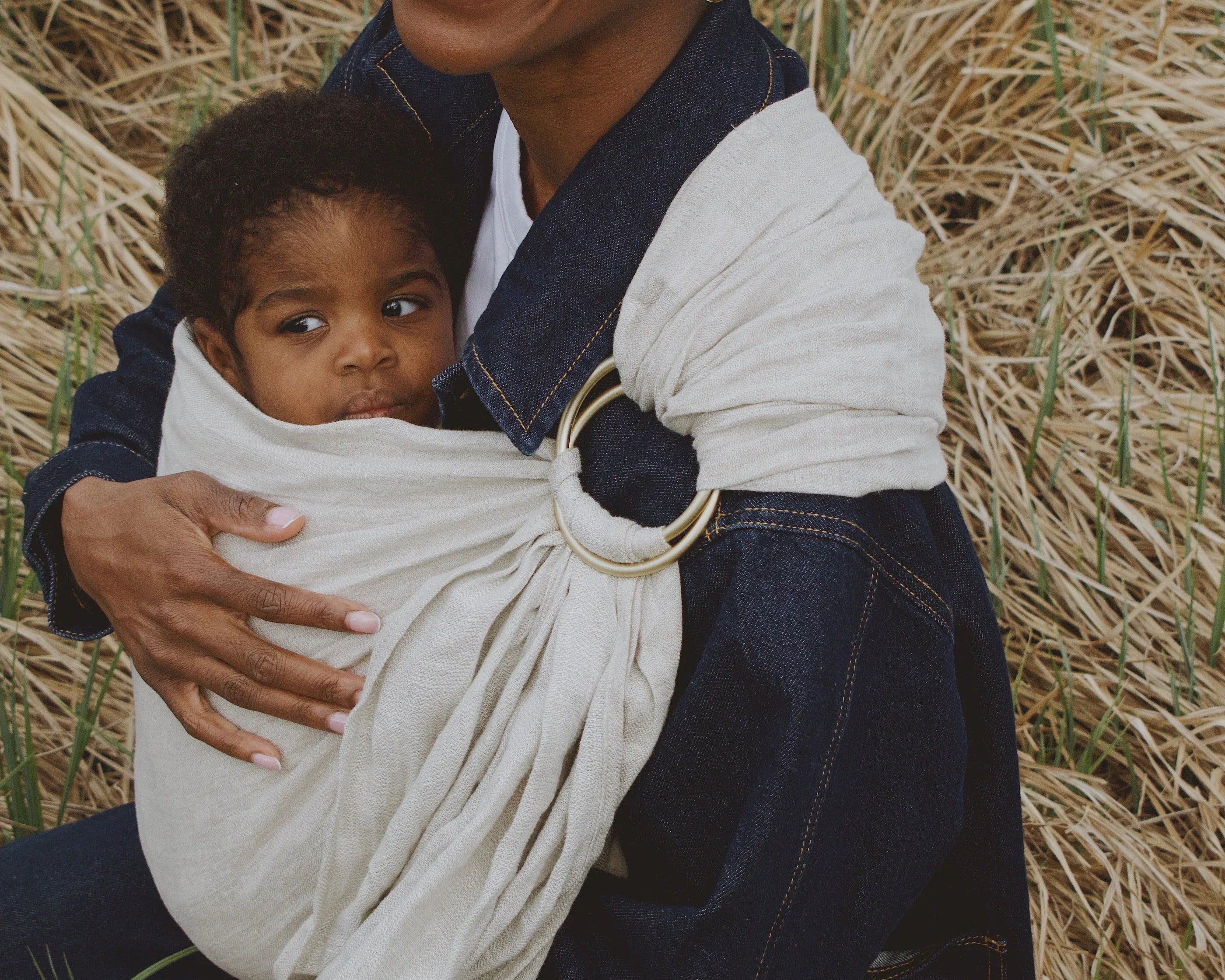 maman souriante qui porte son bébé dans un ring sling gris  
