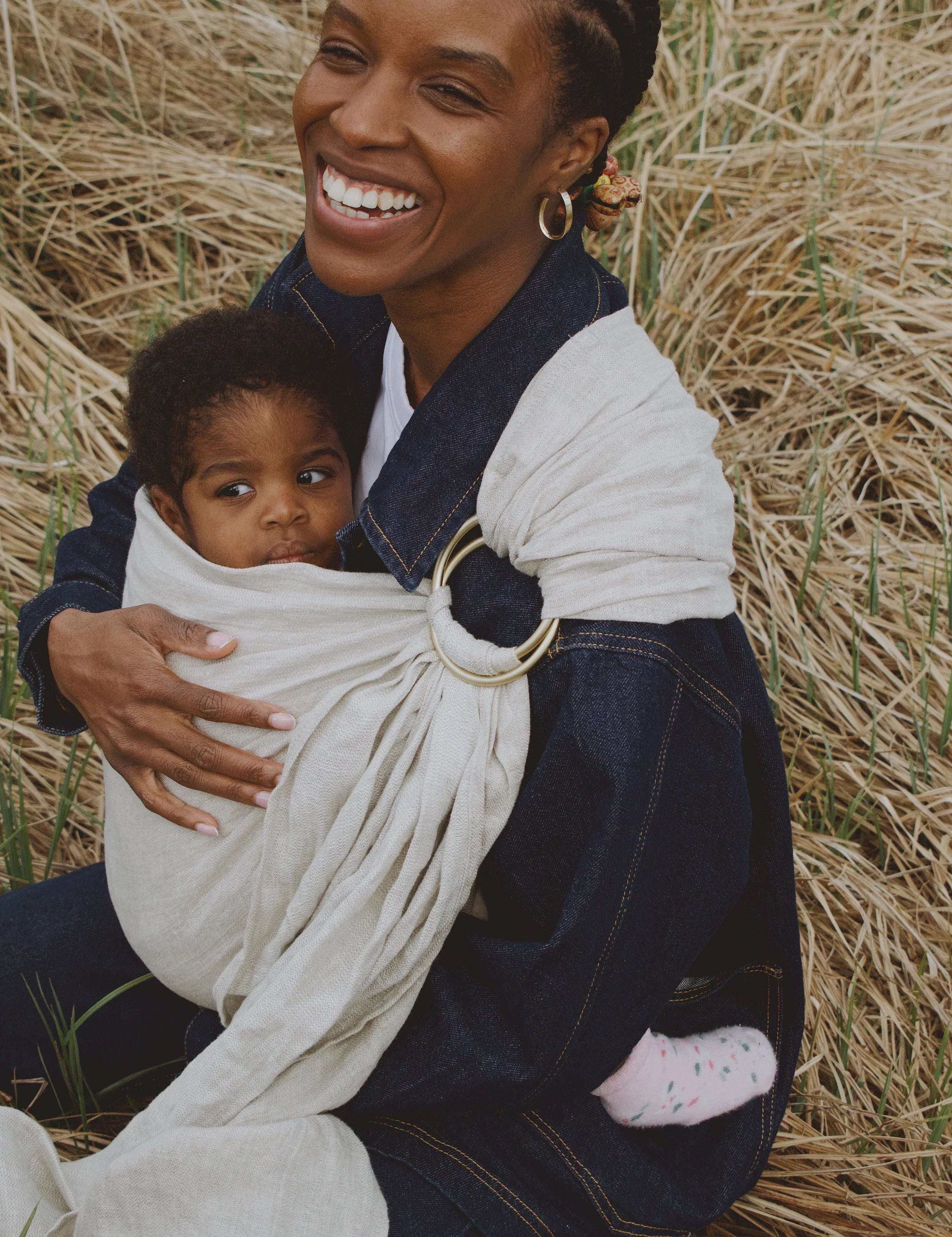 maman souriante qui porte son bébé dans un ring sling gris  