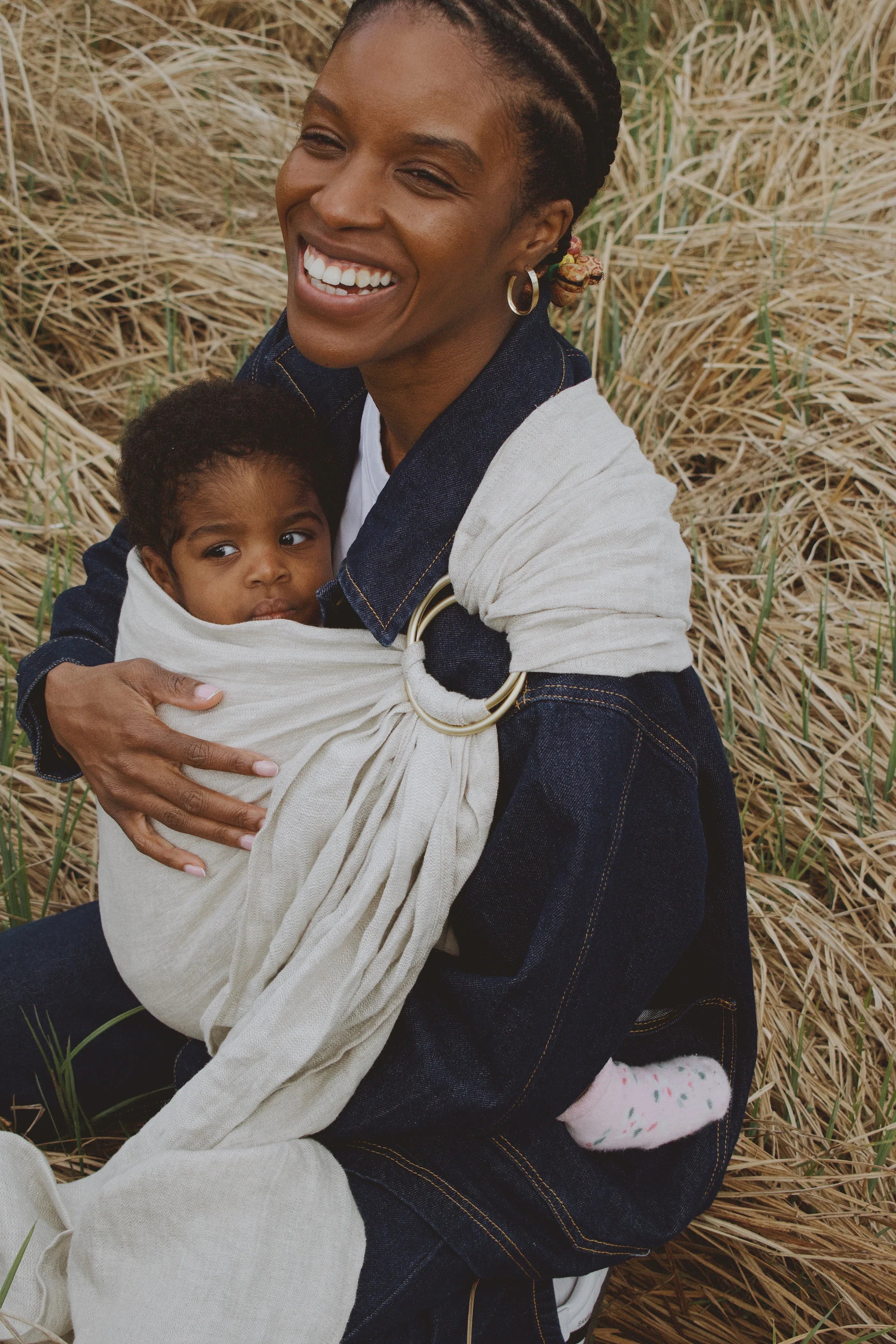 maman souriante qui porte son bébé dans un ring sling gris  
