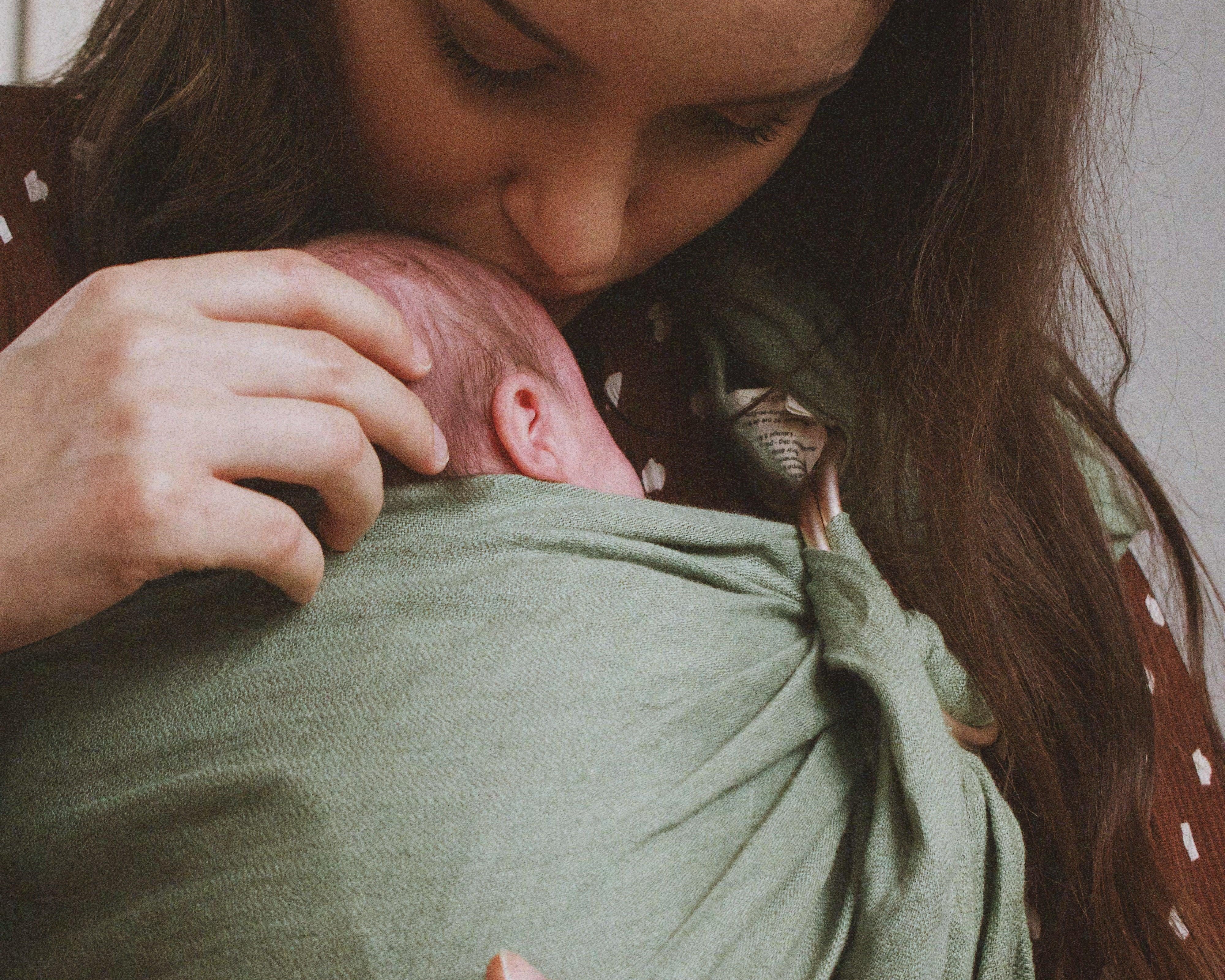 ring sling naissance: maman qui fait un bisous sur son nouveau-né porté dans le sling en lin matcha de Bud & Blossom