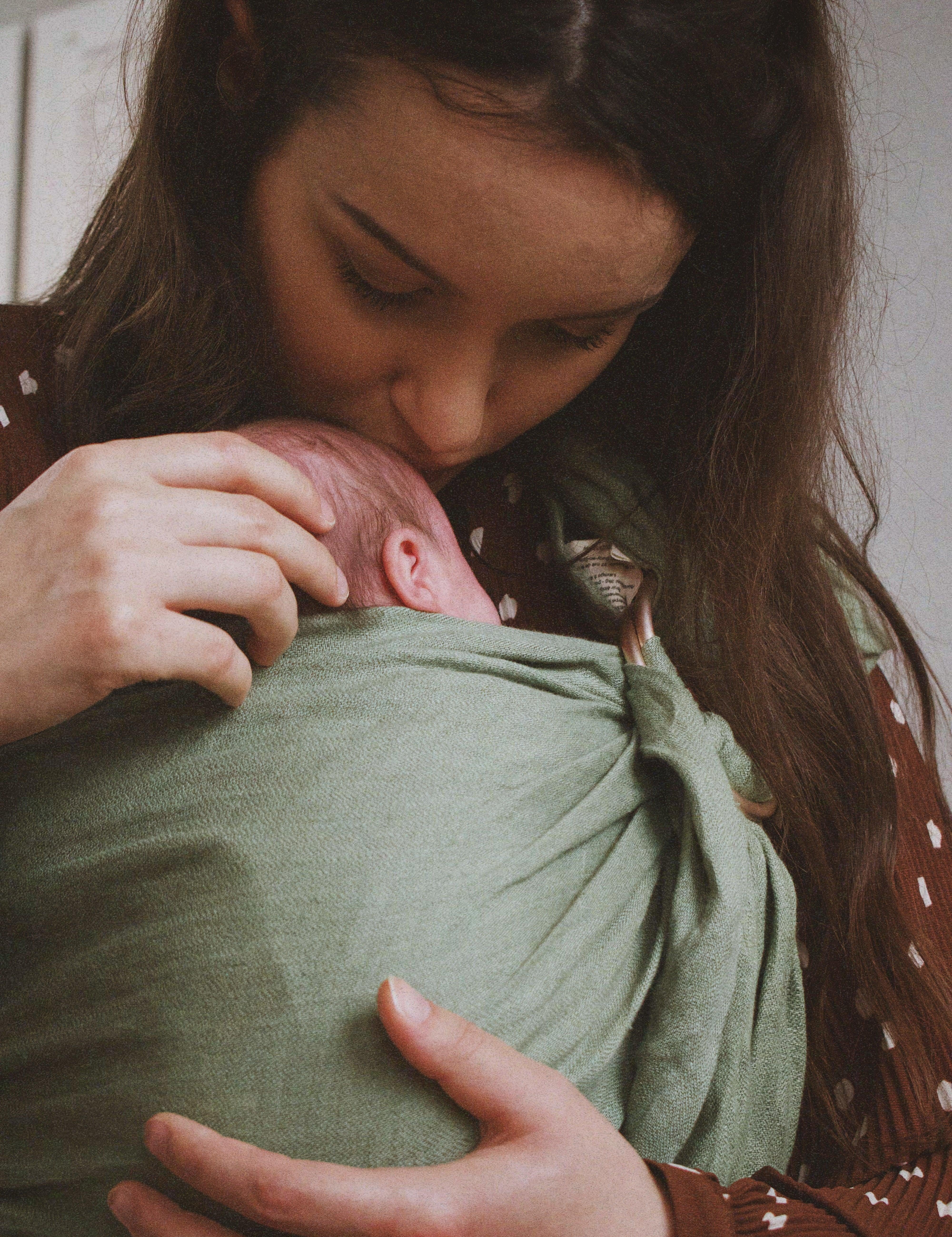 ring sling naissance: maman qui fait un bisous sur son nouveau-né porté dans le sling en lin matcha de Bud & Blossom