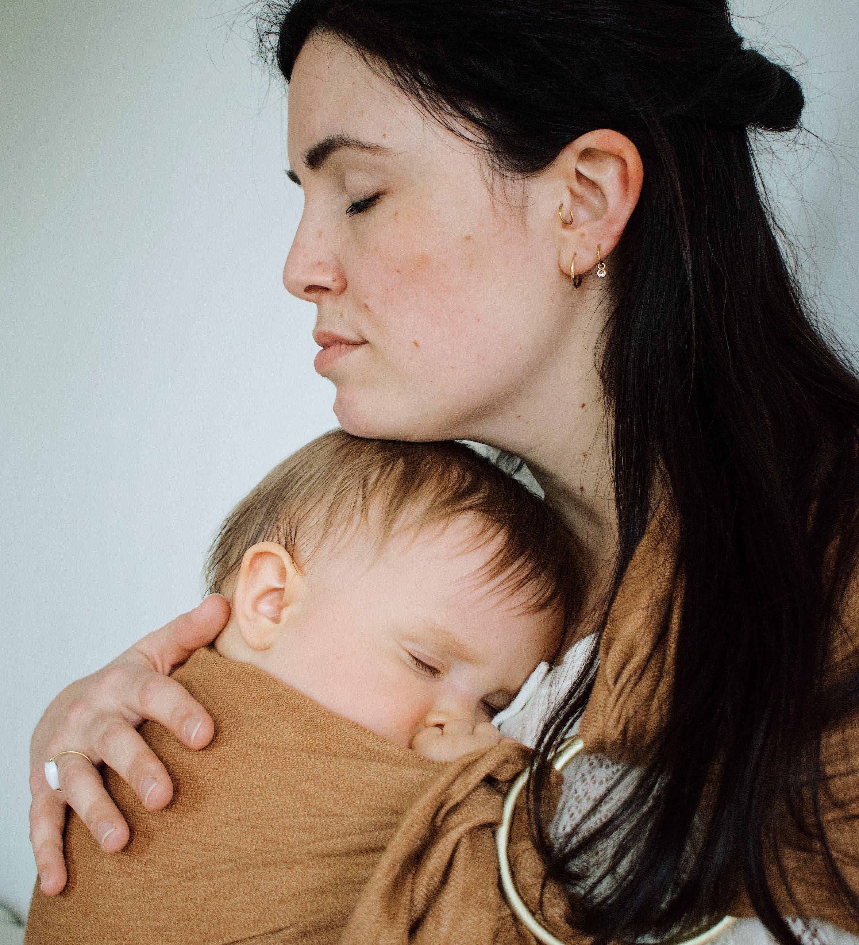 maman qui caresse la tete de son bébé porté de maniere physiologique dans le ring sling de portage coloris camel de la marque Bud & Blossom