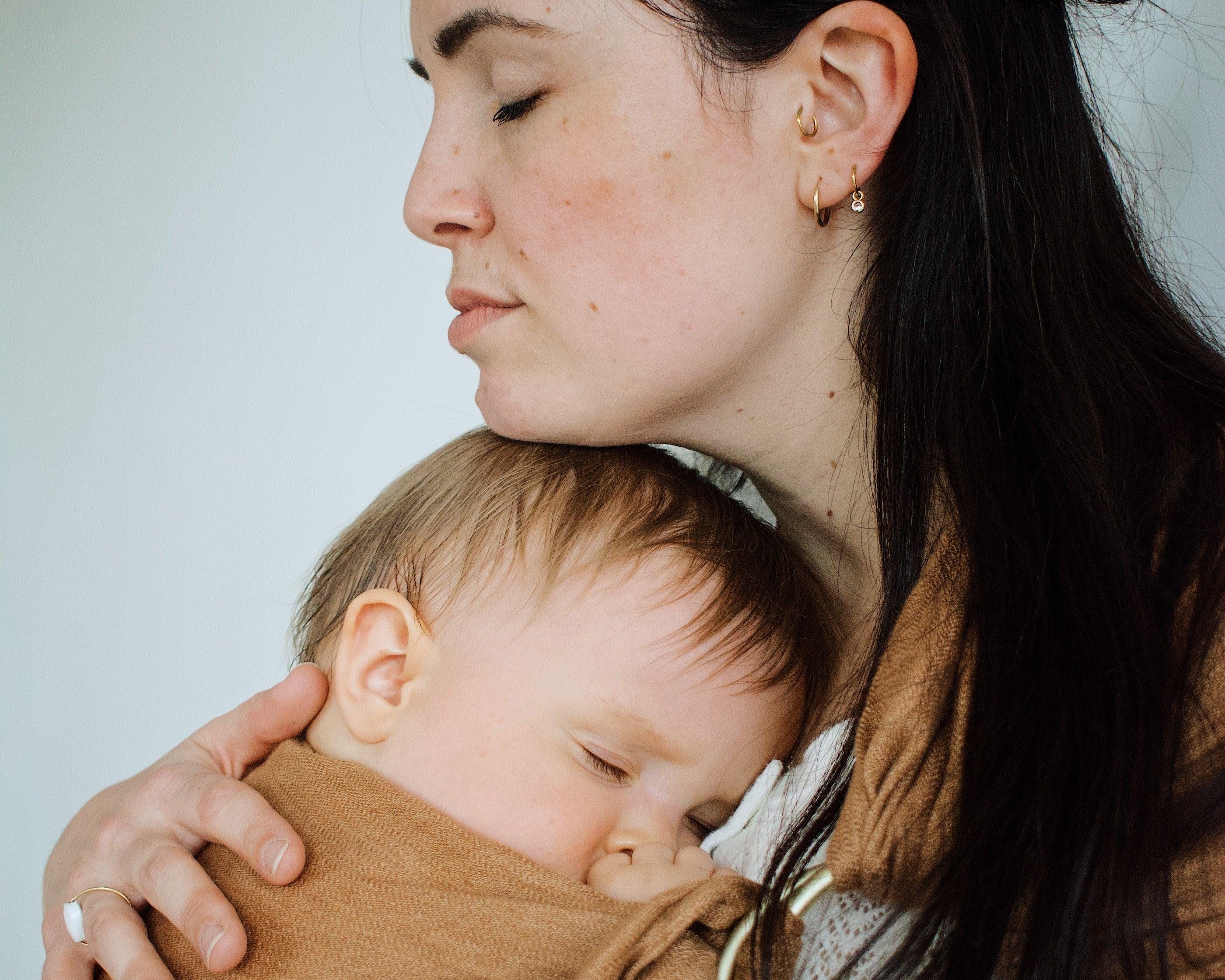 maman qui caresse la tete de son bébé porté de maniere physiologique dans le ring sling de portage coloris camel de la marque Bud & Blossom