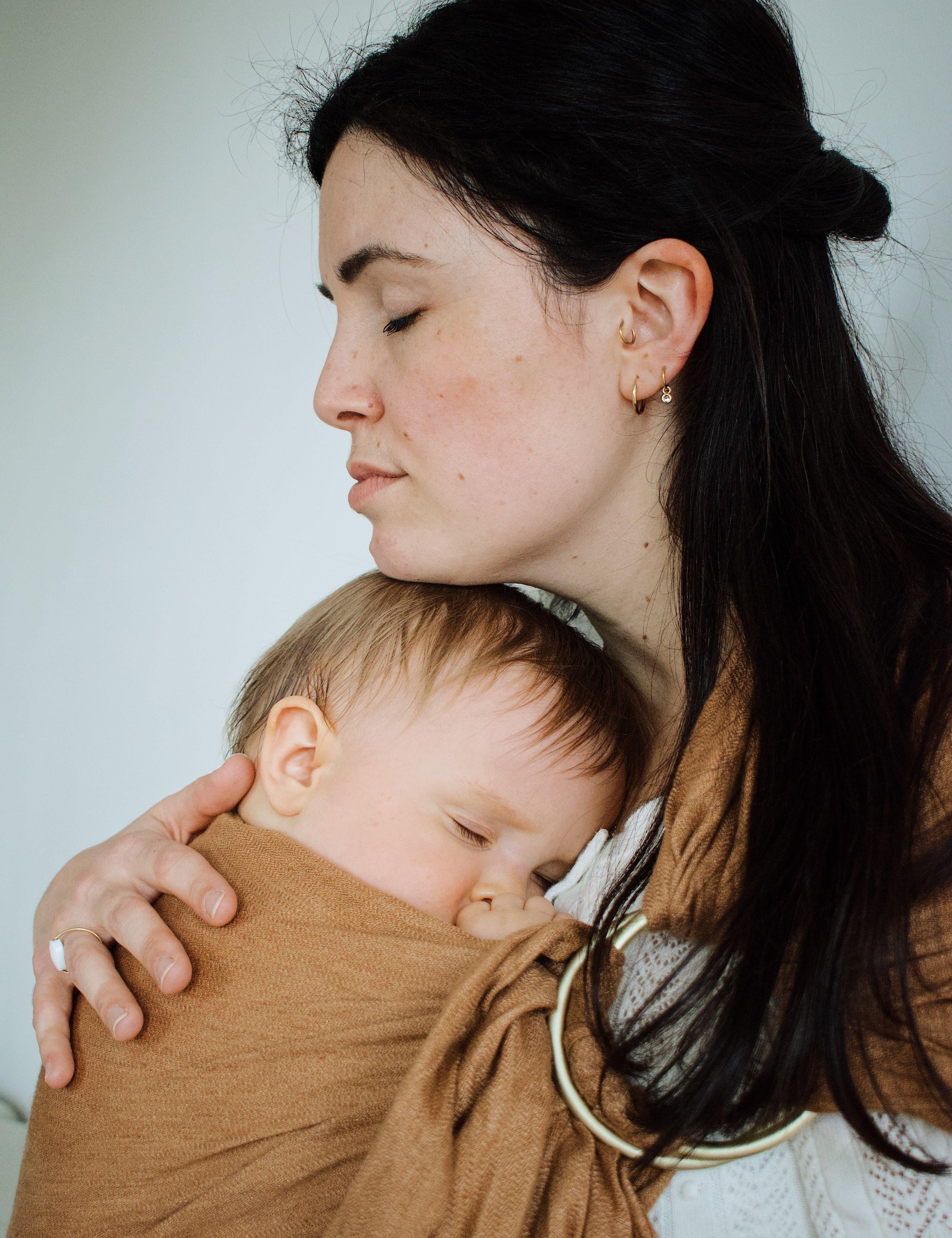 maman qui caresse la tete de son bébé porté de maniere physiologique dans le ring sling de portage coloris camel de la marque Bud & Blossom