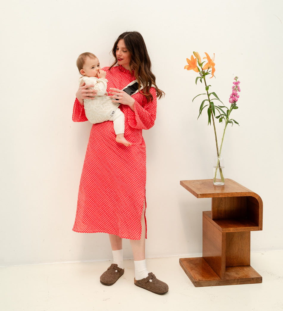 Enfant porté sur la hanche dans un porte-bébé physiologique.