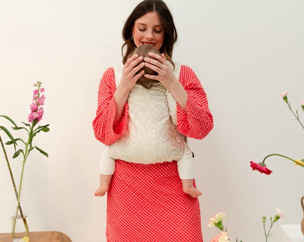 Maman portant son bébé dans un porte-bébé préformé en tissu souple, Exquis Bud & Blossom.