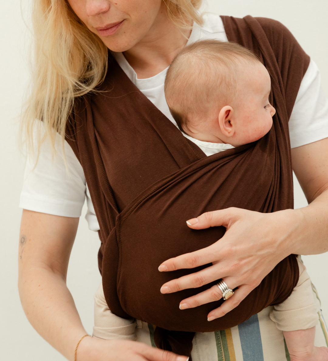 Parent portant son nourrisson contre lui dans un porte-bébé physiologique Bud & Blossom.