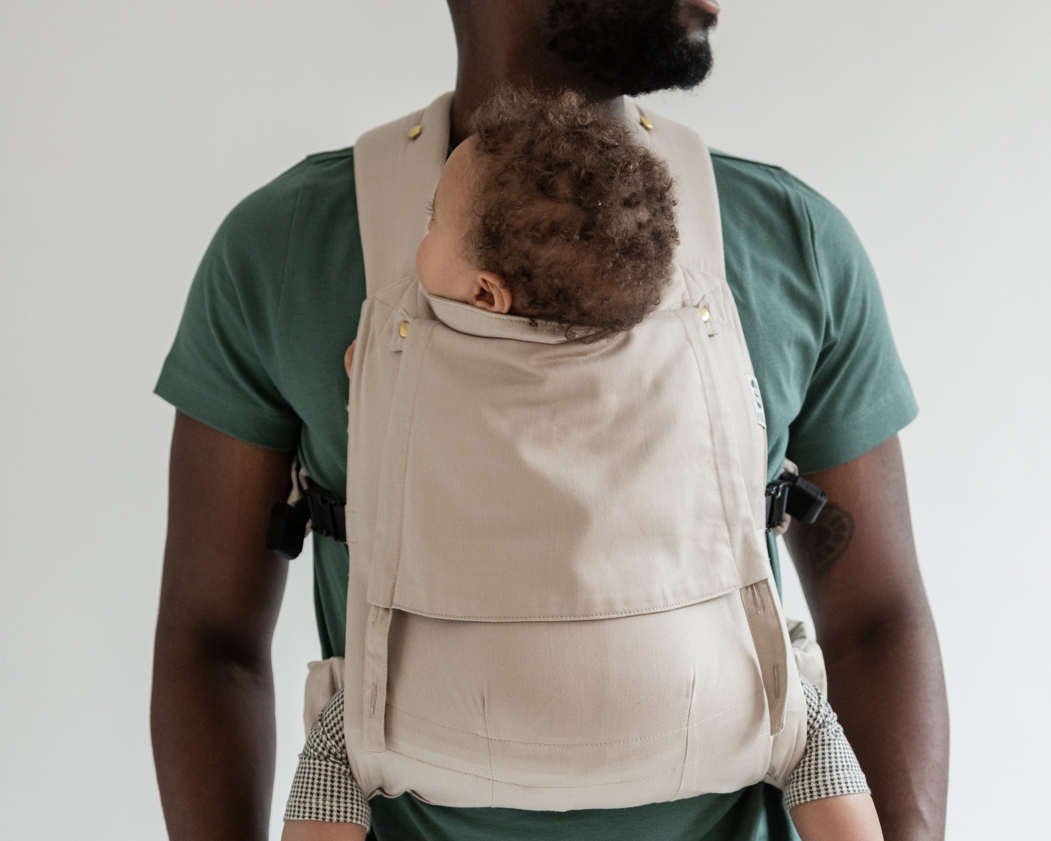 Papa portant son bébé de 8 mois dans le porte-bébé physiologique Exquis coloris taupe, regardant sur le côté