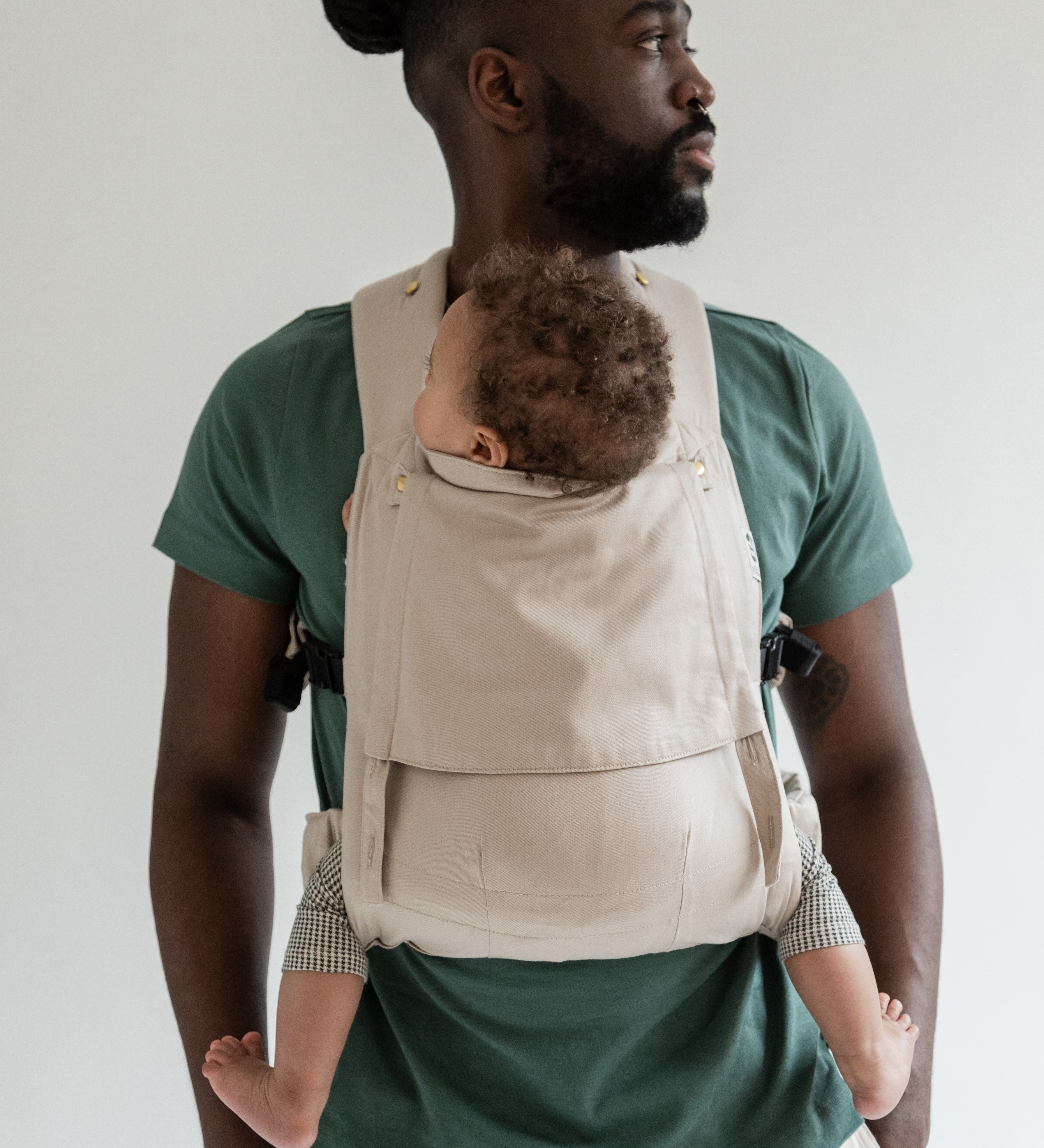 Papa portant son bébé de 8 mois dans le porte-bébé physiologique Exquis coloris taupe, regardant sur le côté