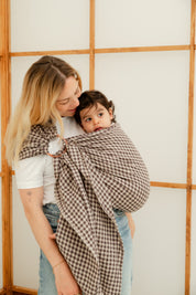 Bébé fille de 2 ans portée dans un sling en lin vichy marron Bud & Blossom, confortable et élégant.