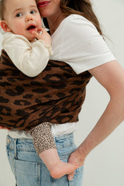Maman portant son bébé contre elle dans un sling en lin motif léopard, vue du coté