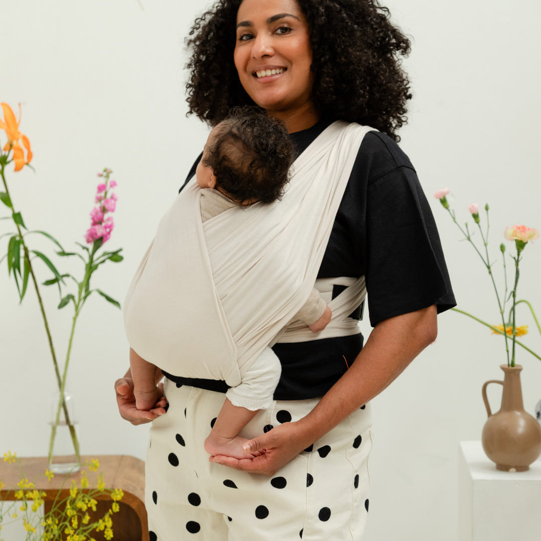 maman portant son bébé grâce au porte-bébé nouveau-né bud and blossom en coton extensible beige